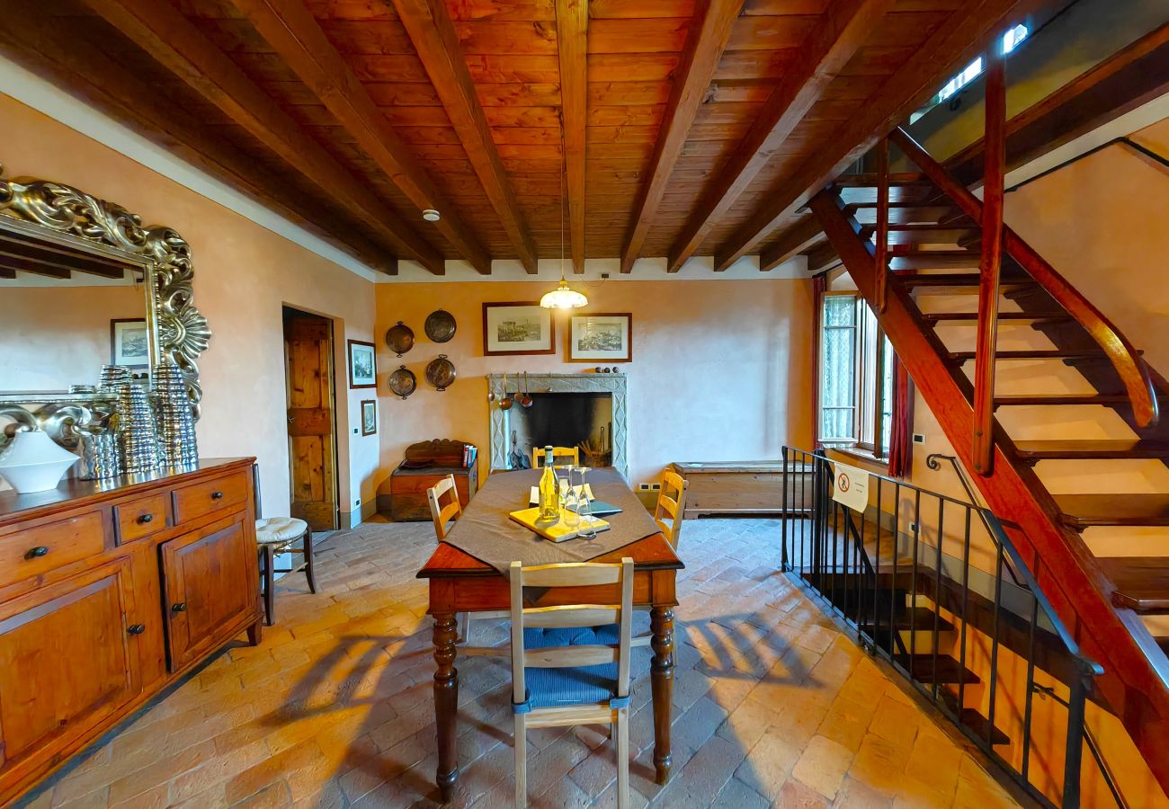 Sala da pranzo con tavolo in legno, camino e soffitto con travi a vista nell’appartamento a Monzambano